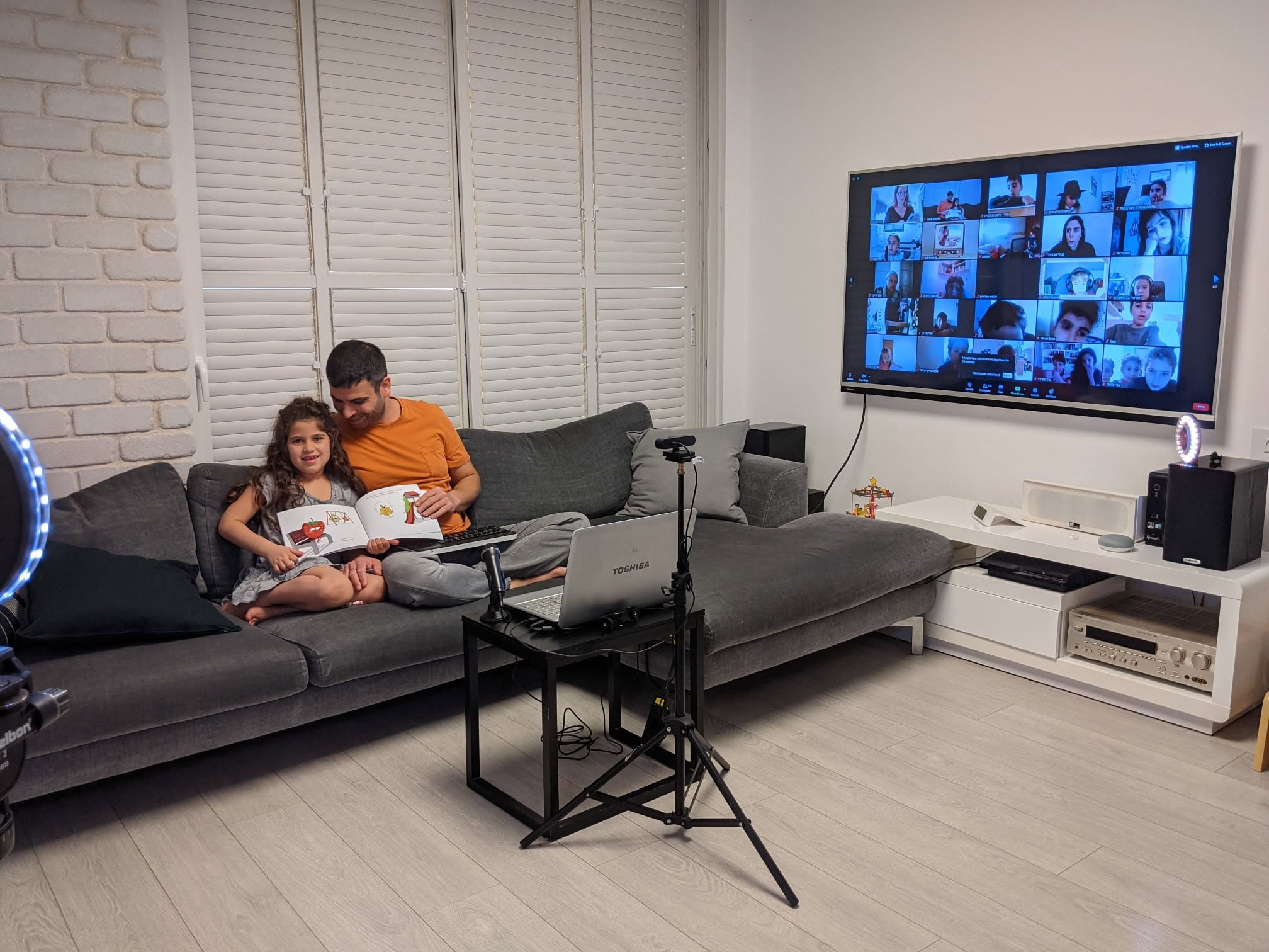 שאול ובתו עם הספר על הספה, מול מסך משתתפי שעת הסיפור בזום